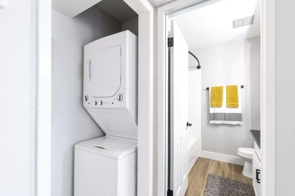 utility closet with stacked washer and dryer looking into bathroom