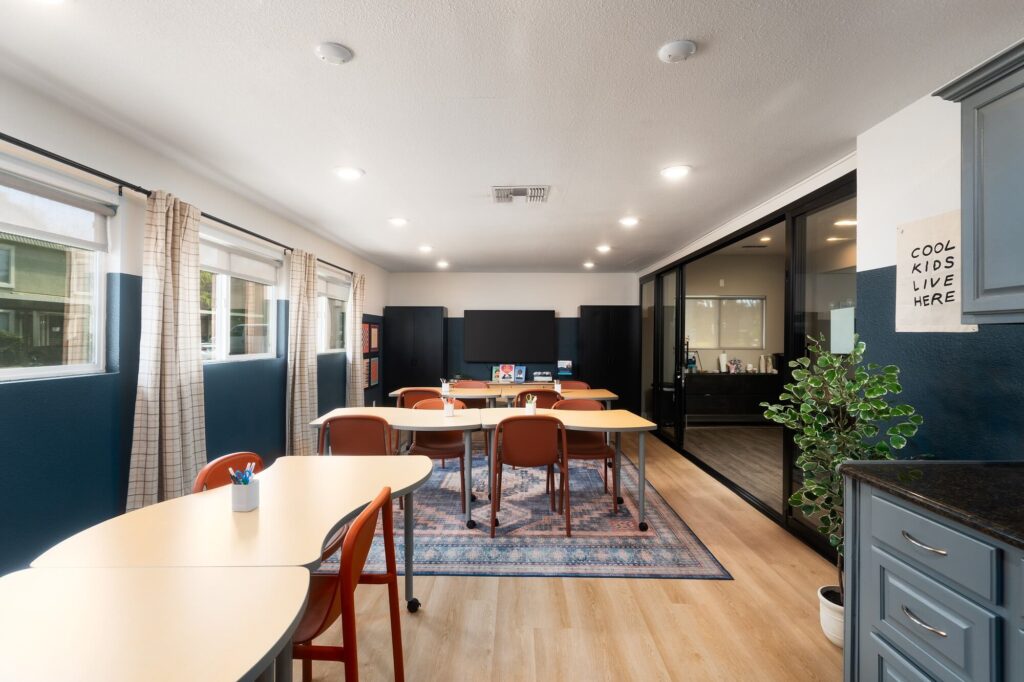 Kids clubhouse with designer lighting, television, table seating, wood-style flooring, and storage lockers